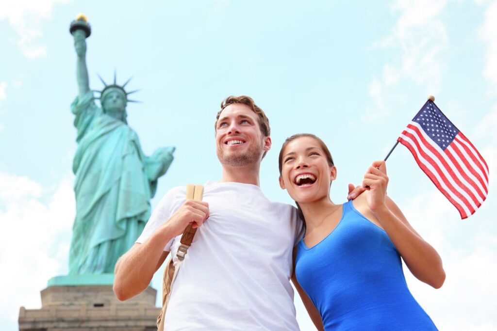 a couple with american flag in front of statue of liberty